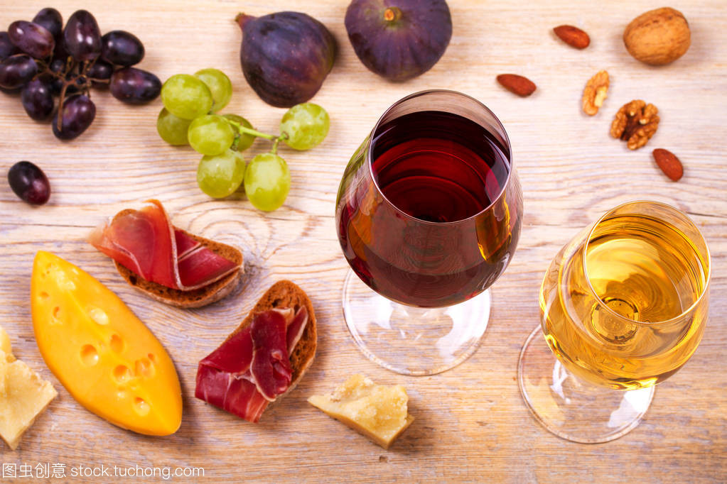 紅色和白色奶酪、 火腿、 無花果和葡萄與葡萄酒杯。木制的桌子上的酒杯。葡萄酒的靜物